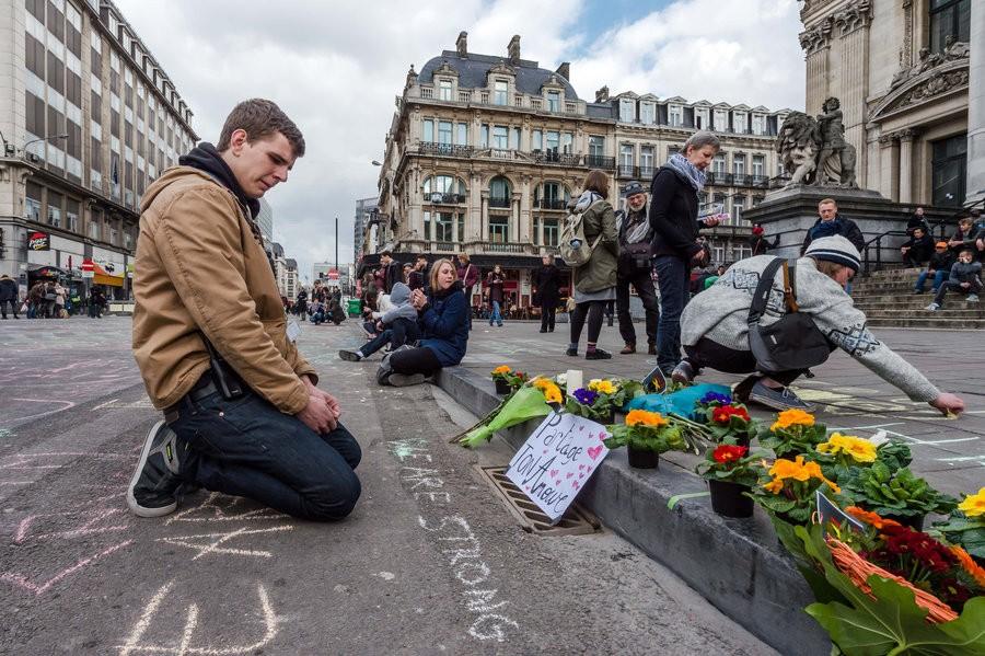 A man looks at flowers and messages of support outside the stock exchange in Brussels (www.npr.org)